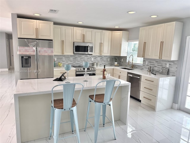 kitchen with visible vents, marble finish floor, stainless steel appliances, a sink, and a kitchen breakfast bar