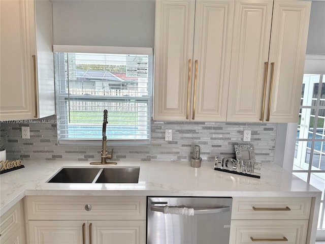 kitchen with stainless steel dishwasher, tasteful backsplash, a sink, and white cabinets