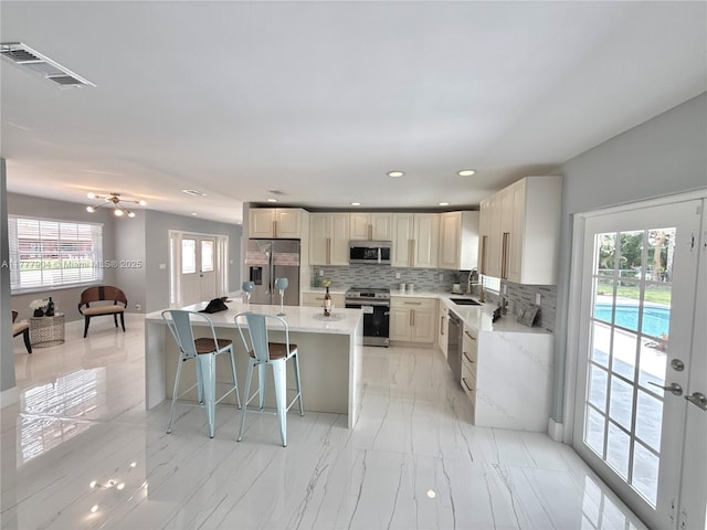 kitchen featuring a sink, a kitchen island, stainless steel appliances, visible vents, and decorative backsplash