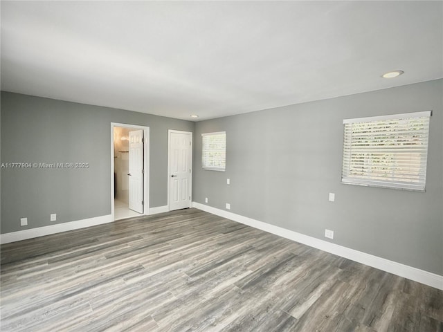 unfurnished bedroom featuring multiple windows, connected bathroom, baseboards, and wood finished floors