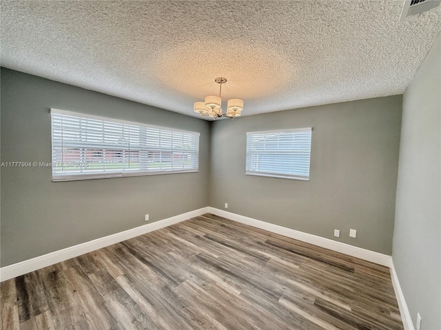 unfurnished room featuring a textured ceiling, visible vents, a chandelier, baseboards, and wood finished floors