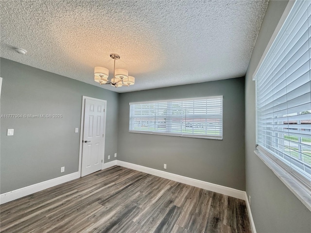 spare room with plenty of natural light, baseboards, a notable chandelier, and dark wood-style flooring