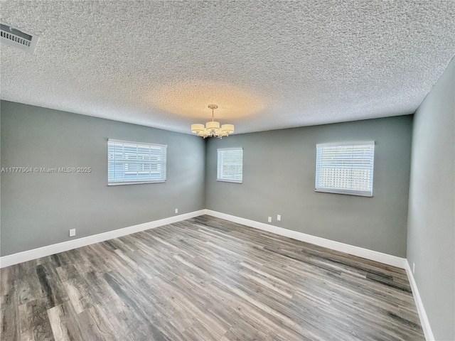 empty room with wood finished floors, a textured ceiling, baseboards, visible vents, and an inviting chandelier