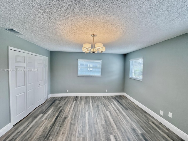 unfurnished dining area with an inviting chandelier, wood finished floors, baseboards, and visible vents