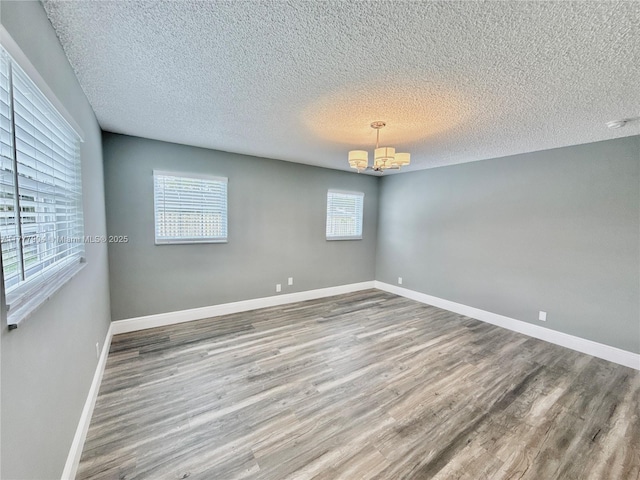 empty room with an inviting chandelier, a textured ceiling, baseboards, and wood finished floors