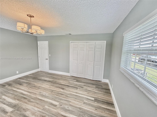 unfurnished bedroom featuring a closet, wood finished floors, a textured ceiling, baseboards, and an inviting chandelier