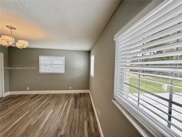 empty room featuring a notable chandelier, dark wood-type flooring, baseboards, and a textured ceiling