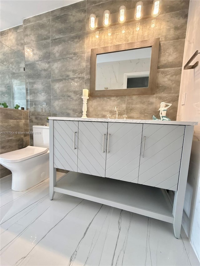bathroom featuring tile walls, marble finish floor, toilet, and vanity