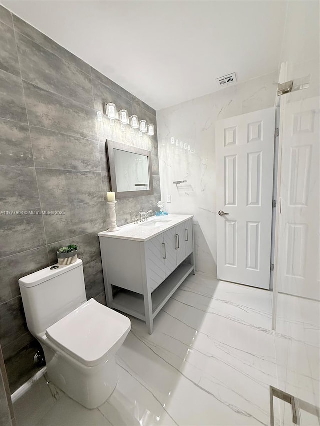 bathroom featuring vanity, tile walls, toilet, marble finish floor, and visible vents