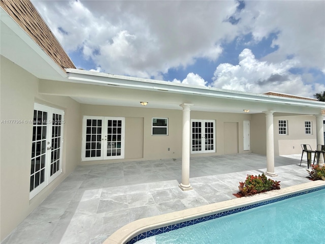 rear view of property with stucco siding, an outdoor pool, a patio area, and french doors
