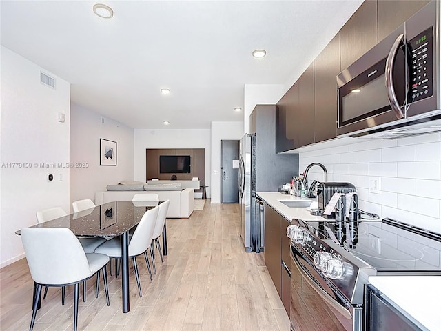 kitchen with visible vents, stainless steel appliances, light wood-type flooring, modern cabinets, and backsplash