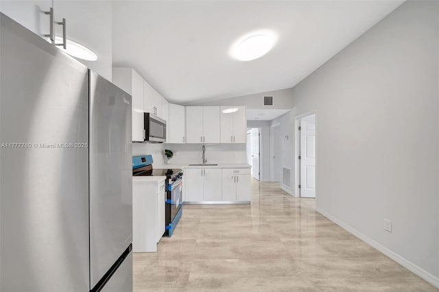 kitchen with vaulted ceiling, white cabinets, appliances with stainless steel finishes, light countertops, and a sink