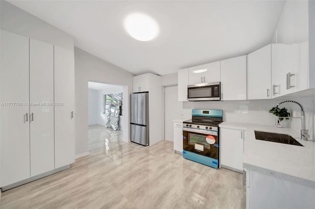 kitchen featuring tasteful backsplash, white cabinetry, vaulted ceiling, a sink, and stainless steel appliances