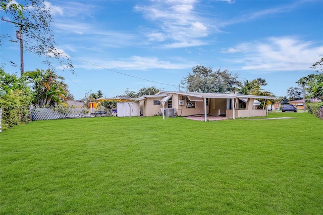 rear view of property featuring central AC, a patio area, a lawn, fence, and stucco siding