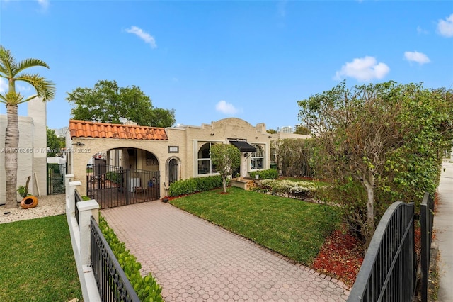 mediterranean / spanish-style house featuring a tiled roof, a fenced front yard, stucco siding, a front yard, and a gate