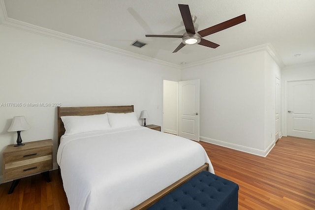 bedroom with ornamental molding, baseboards, visible vents, and wood finished floors