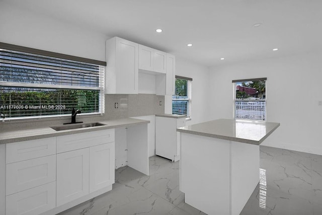kitchen with recessed lighting, a kitchen island, marble finish floor, a sink, and white cabinetry