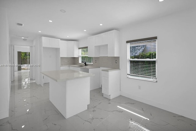 kitchen with recessed lighting, a sink, marble finish floor, a kitchen island, and white cabinetry