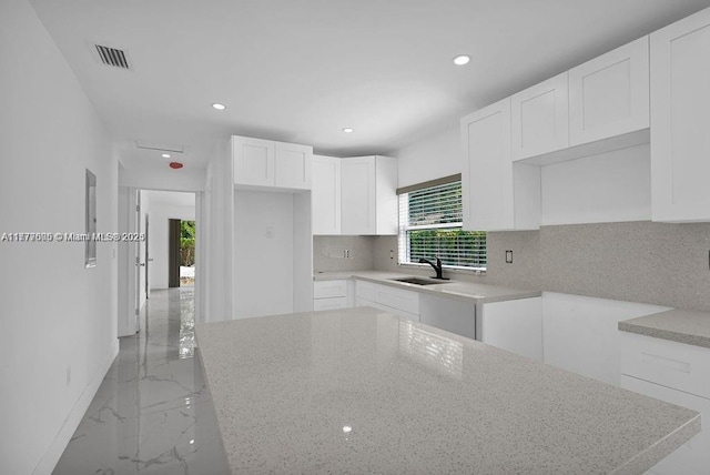 kitchen featuring light stone countertops, marble finish floor, decorative backsplash, and a sink
