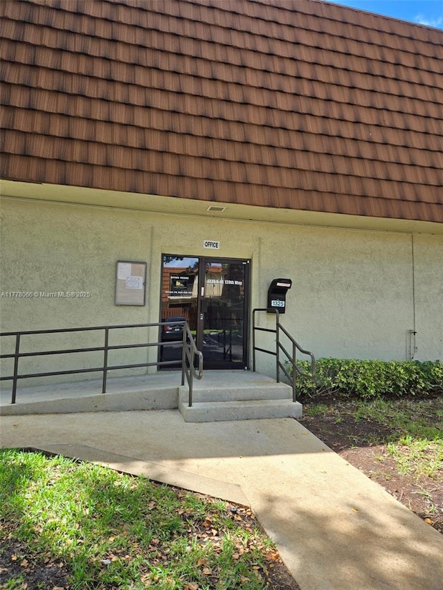 entrance to property featuring mansard roof, a tile roof, and stucco siding