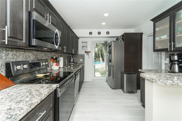 kitchen with stainless steel appliances, a sink, tasteful backsplash, light wood-style floors, and light stone counters
