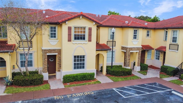 townhome / multi-family property featuring a tiled roof, stucco siding, and stone siding