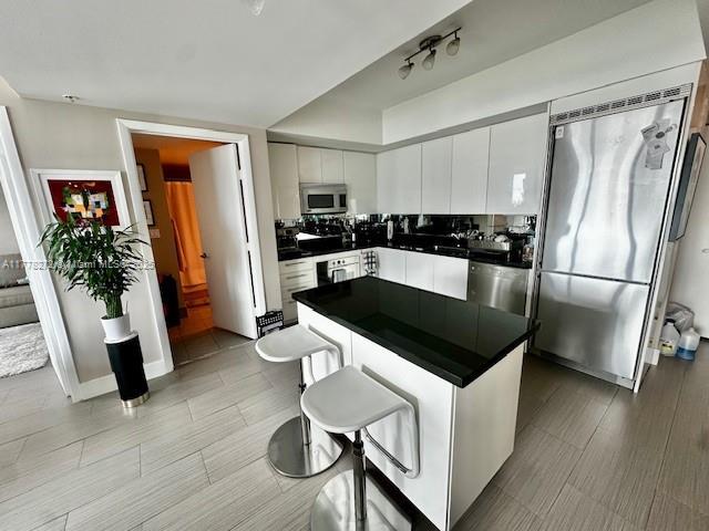 92 SW 3rd St Unit 4104, Miami, FL 33130 - kitchen featuring appliances with stainless steel finishes, dark countertops, white cabinetry, a center island, and a breakfast bar area