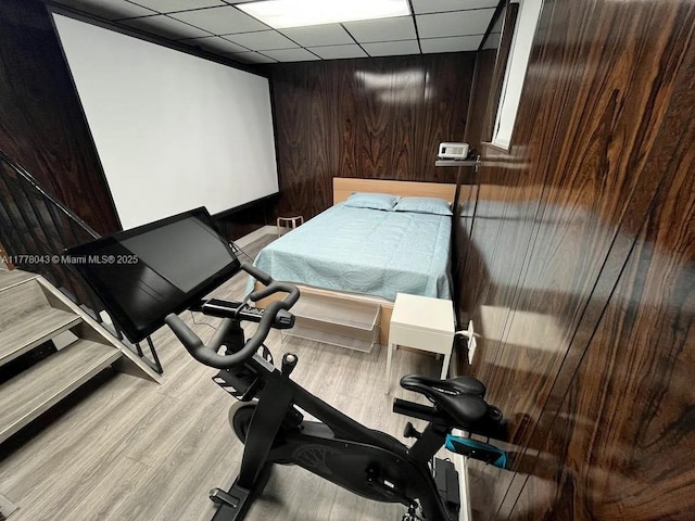 exercise area featuring wood walls, a paneled ceiling, and light wood finished floors