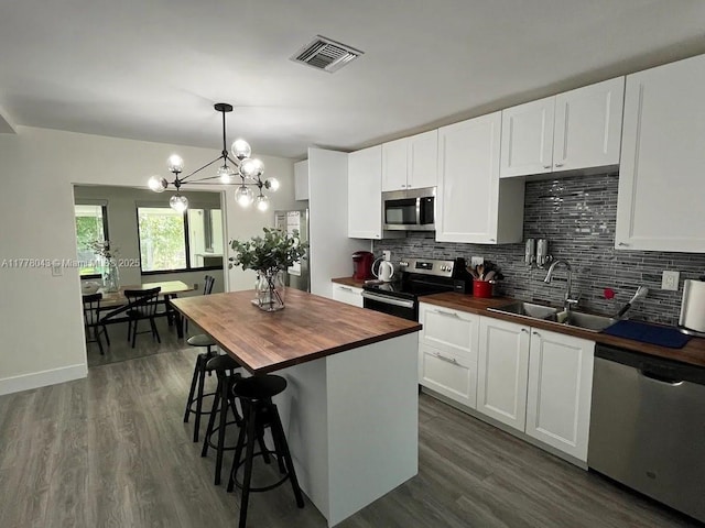 kitchen featuring visible vents, wood counters, stainless steel appliances, a sink, and a notable chandelier