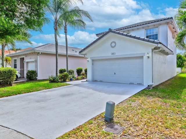 view of front of property featuring driveway, an attached garage, a tiled roof, and stucco siding