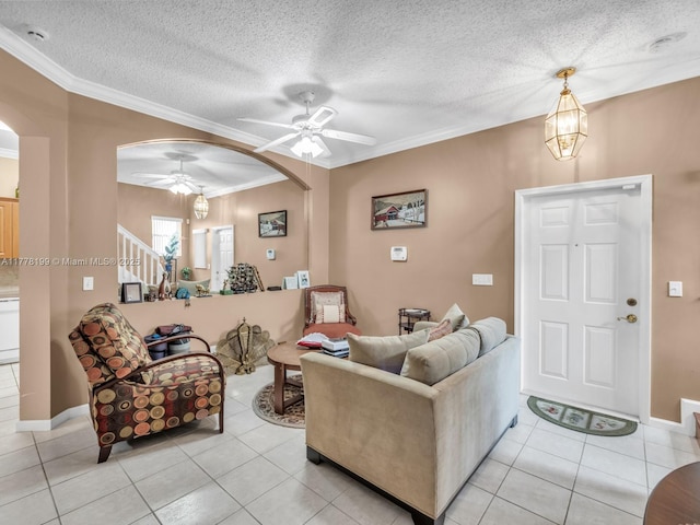 living area featuring arched walkways, a textured ceiling, ornamental molding, and a ceiling fan