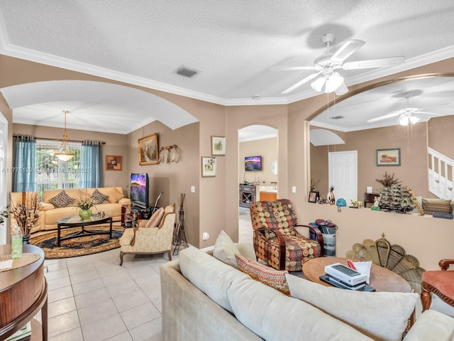 living area with crown molding, a ceiling fan, a textured ceiling, light tile patterned floors, and arched walkways