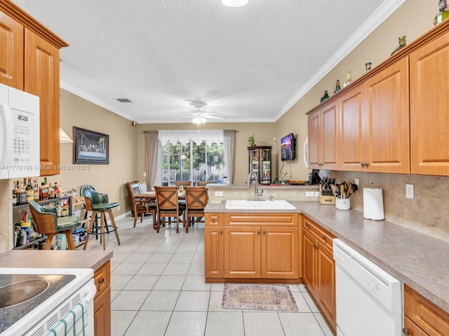 kitchen with light tile patterned floors, a peninsula, a sink, and white appliances