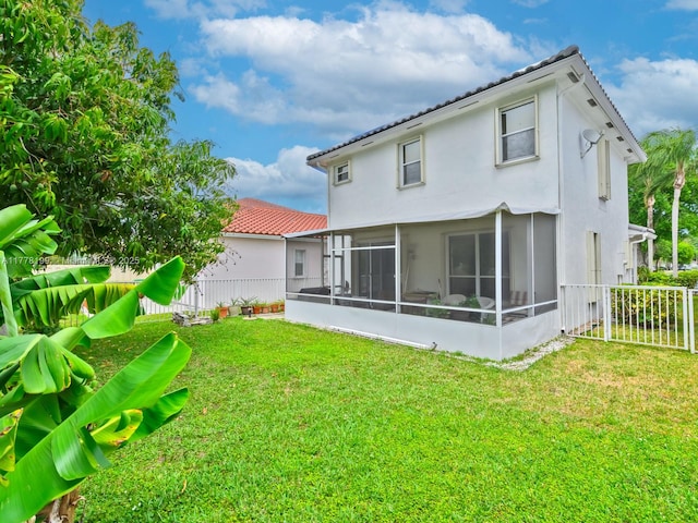 back of property with a sunroom, fence, stucco siding, and a yard