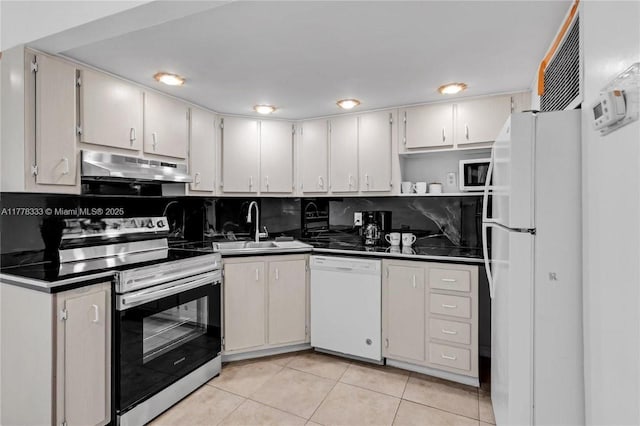 kitchen with dark countertops, a sink, light tile patterned floors, under cabinet range hood, and white appliances