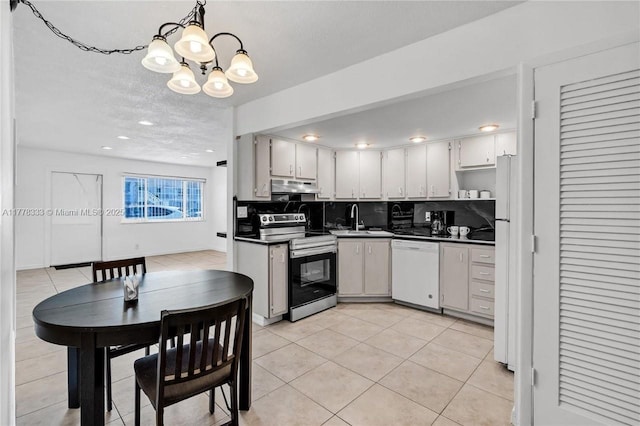 kitchen featuring dark countertops, white appliances, under cabinet range hood, a chandelier, and a sink
