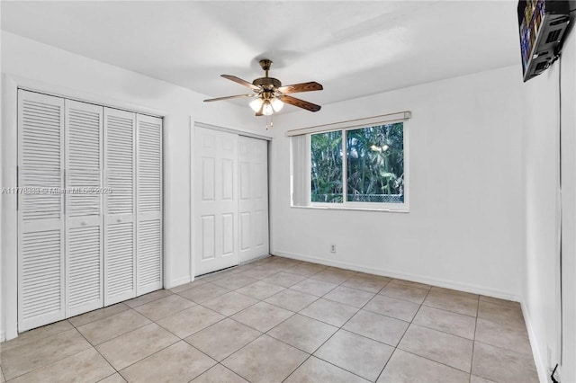 unfurnished bedroom with baseboards, a ceiling fan, multiple closets, and light tile patterned flooring