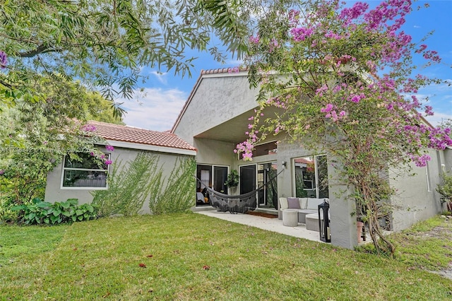 rear view of property featuring a tiled roof, an outdoor living space, a lawn, a patio, and stucco siding