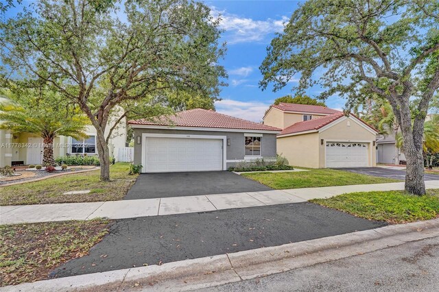 view of front of house with stucco siding, a front yard, a tile roof, and aphalt driveway
