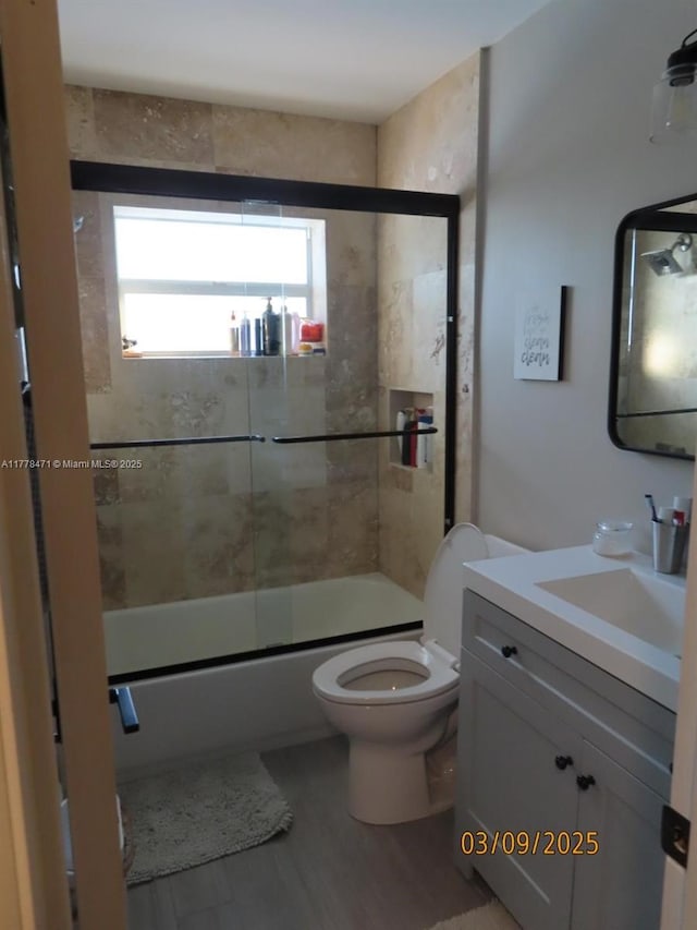 full bathroom featuring toilet, vanity, bath / shower combo with glass door, and wood finished floors