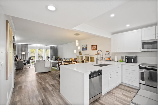 kitchen featuring light countertops, a sink, a peninsula, open floor plan, and stainless steel appliances