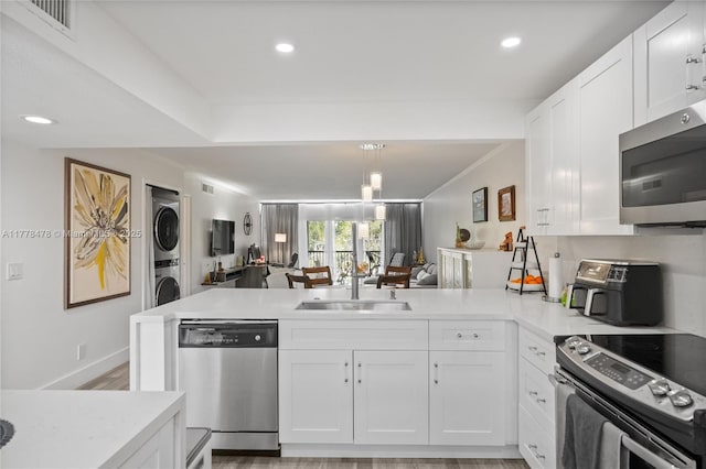 kitchen featuring light countertops, stacked washer and clothes dryer, stainless steel appliances, a sink, and a peninsula