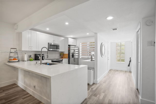 kitchen with light countertops, a peninsula, appliances with stainless steel finishes, a sink, and light wood-style floors