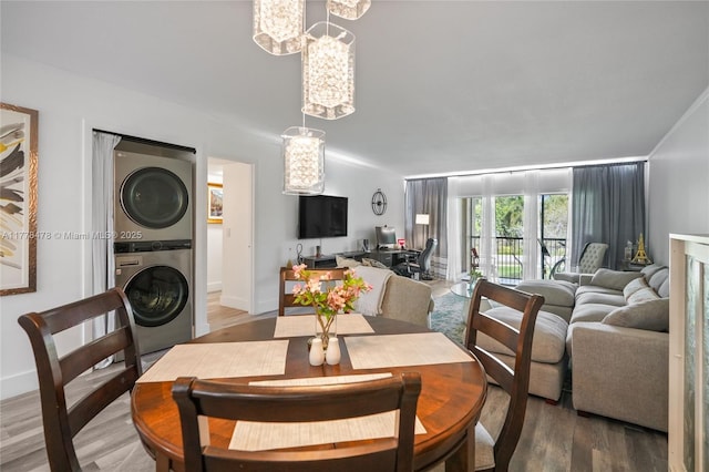 dining area with baseboards, wood finished floors, stacked washing maching and dryer, and a notable chandelier