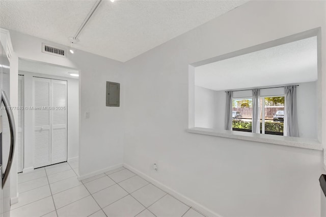 unfurnished room with electric panel, a textured ceiling, light tile patterned floors, baseboards, and visible vents