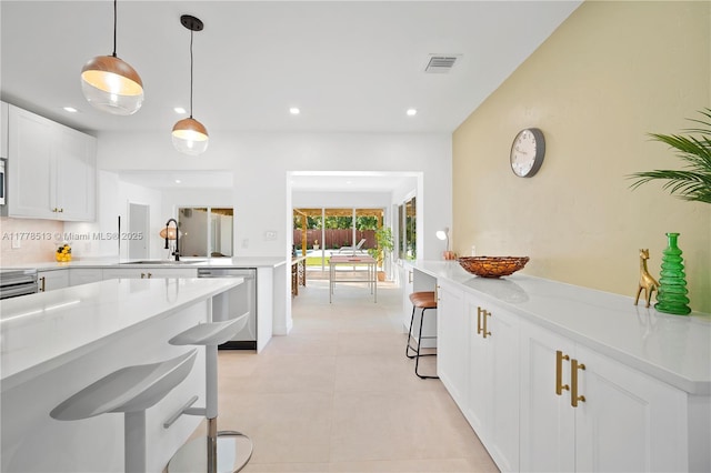kitchen with visible vents, a sink, light countertops, stainless steel dishwasher, and a breakfast bar area