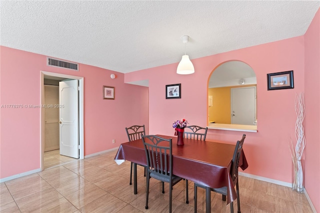 dining area with arched walkways, baseboards, visible vents, and a textured ceiling