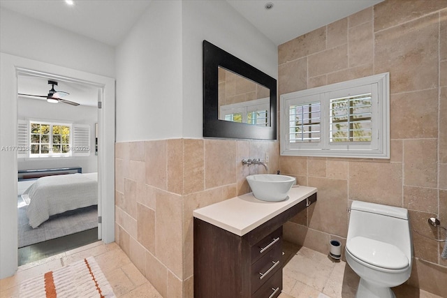 bathroom featuring toilet, ceiling fan, tile walls, connected bathroom, and vanity