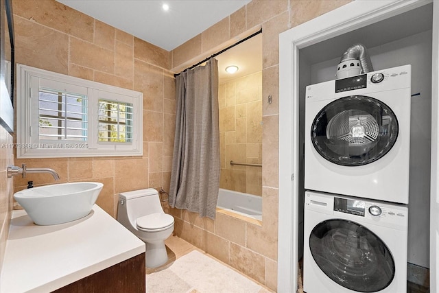 full bath featuring vanity, stacked washer and clothes dryer, toilet, tiled shower / bath combo, and tile walls