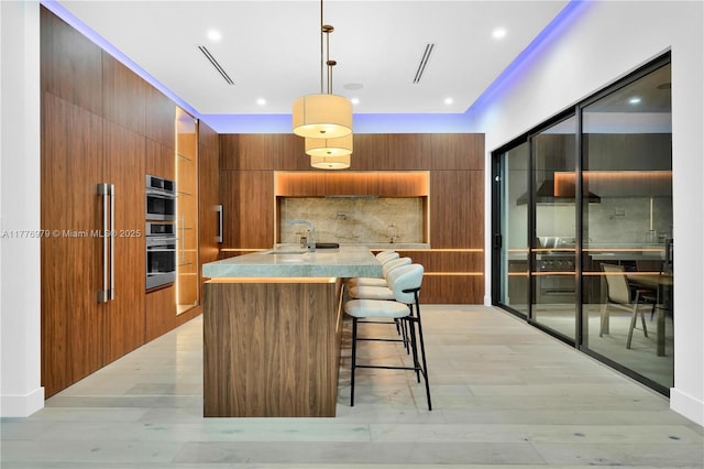 kitchen featuring brown cabinetry, decorative backsplash, modern cabinets, and light wood finished floors